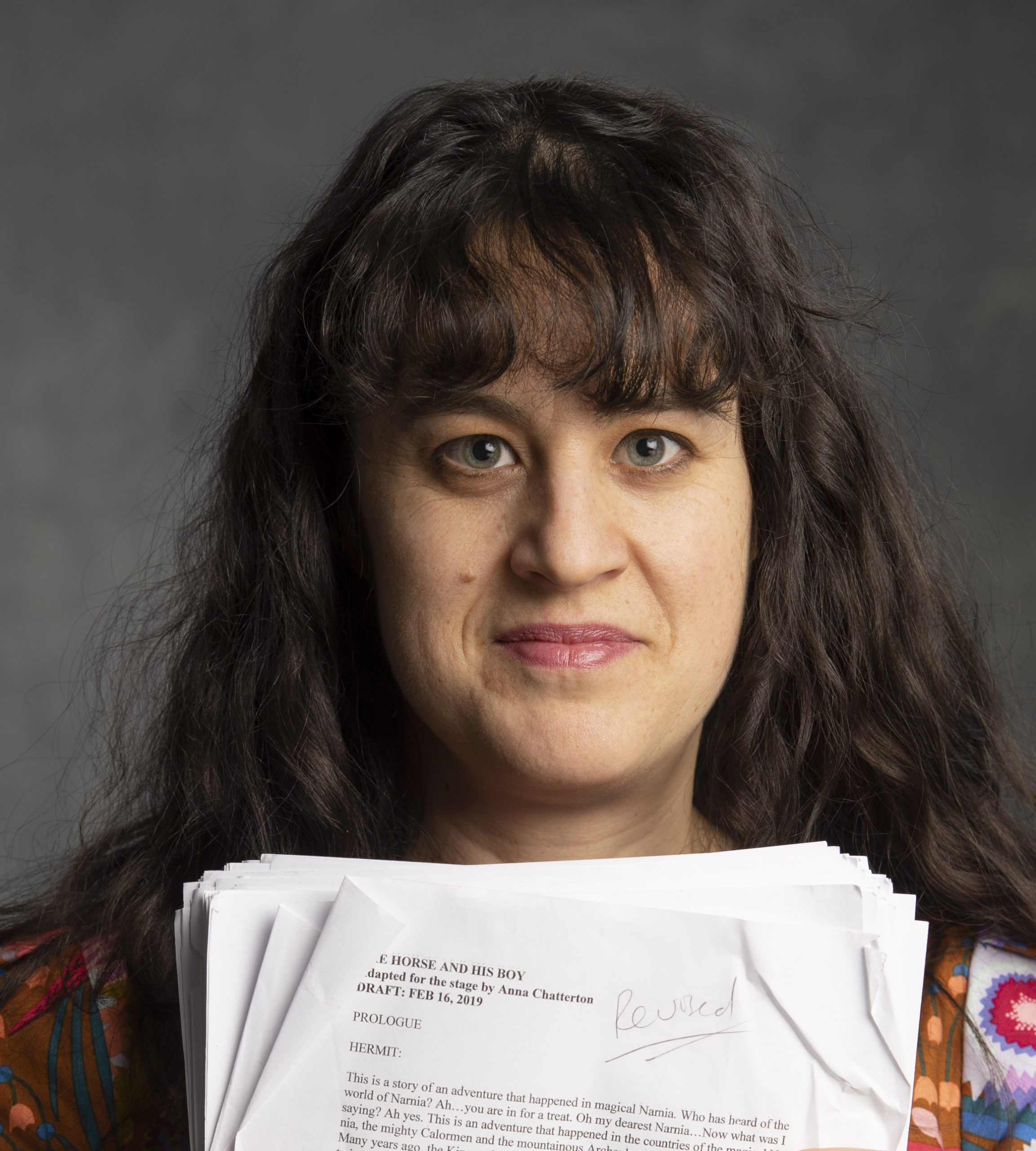 Portrait of a person with long wavy dark hair with bangs holding script paper