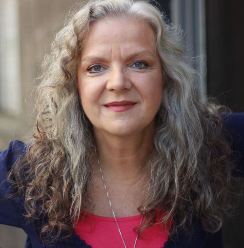 Portrait of person with long curly silver hair with black and pink top