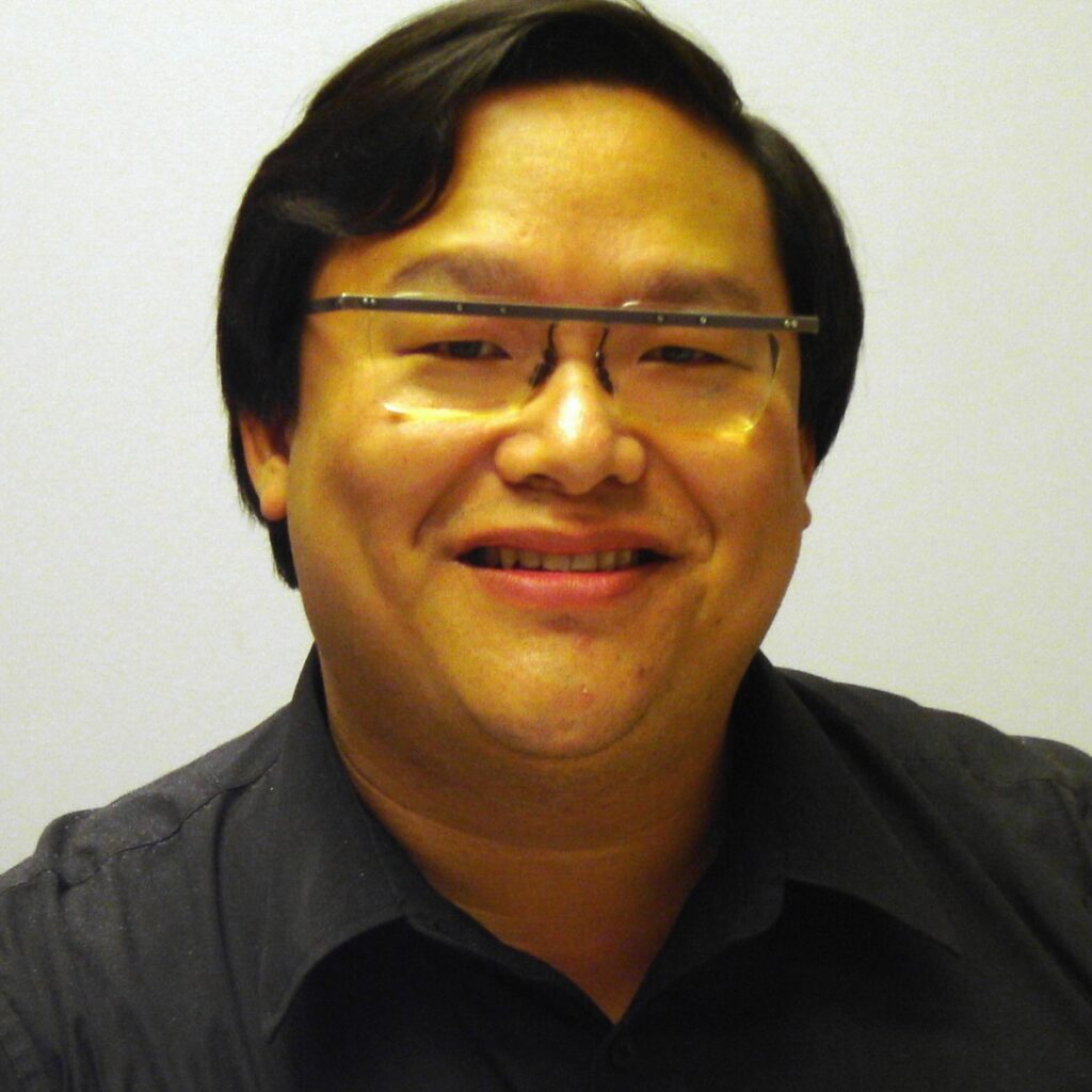 Man with dark hair, glasses, and black shirt smiling in front of white background.