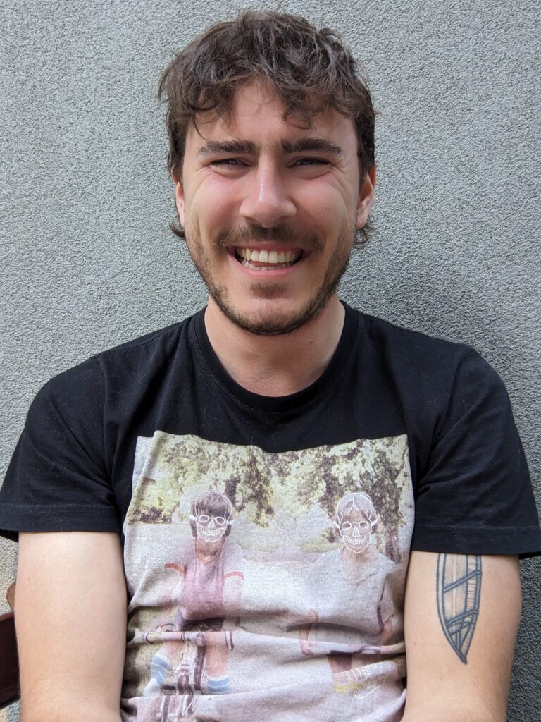 Man with curly brown hair and black graphic t-shirt smiling