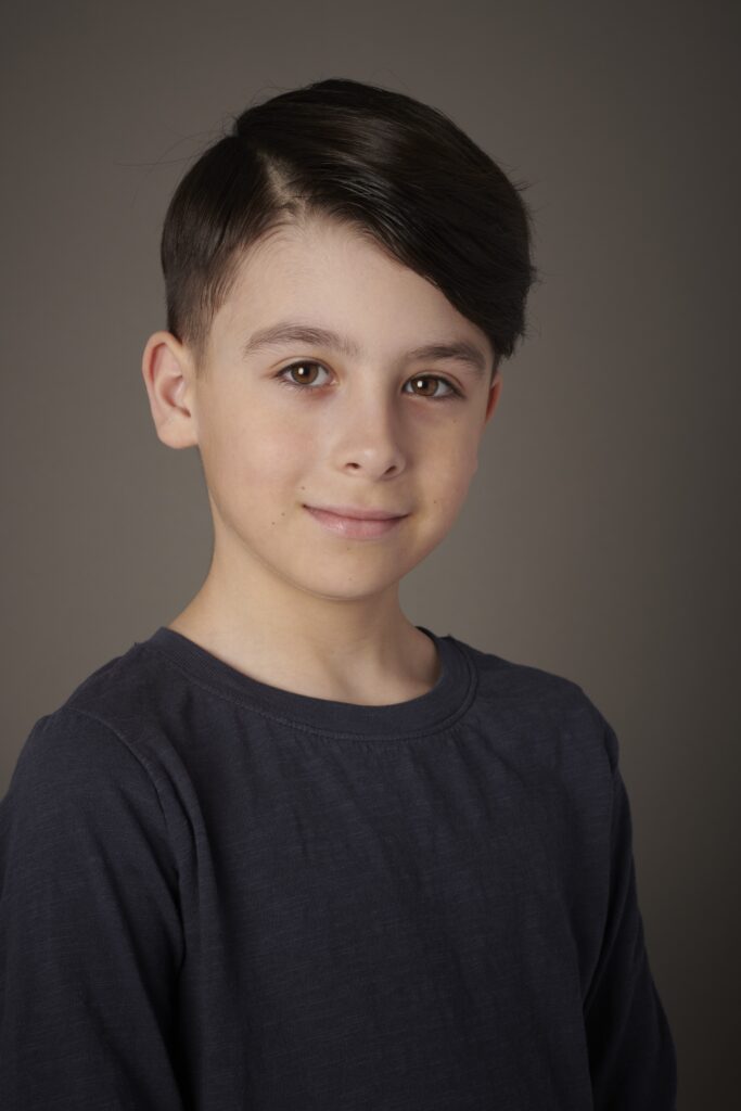 Studio portrait of a young child with combed over dark hair and dark blue long sleeve top