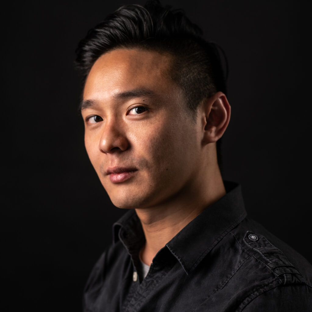 Studio portrait of a man angled to the left in a black shirt with dark hair. Photo by Dahlia Katz