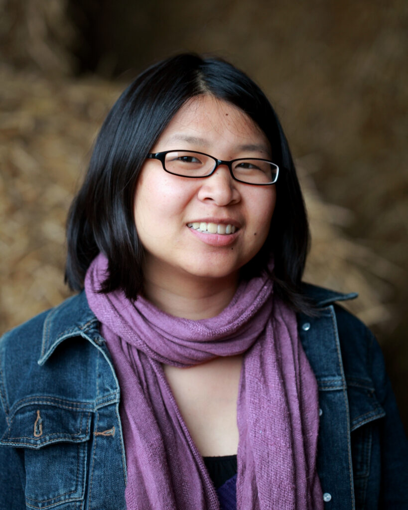 Person with shoulder length black hair, blue jean jacket, and purple scarf