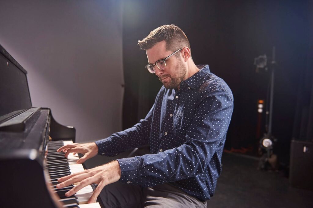 Main in blue shirt and glasses playing on the piano