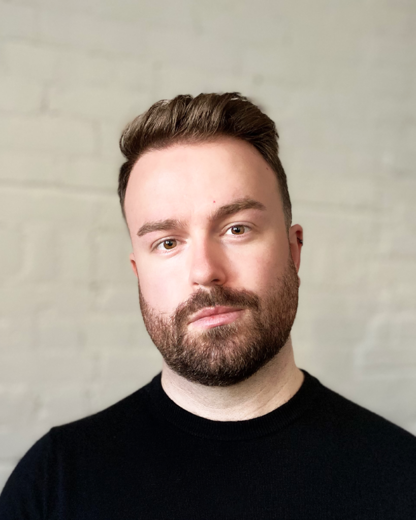 Image of man wearing a black shirt with brown bears and short quiffed hair.