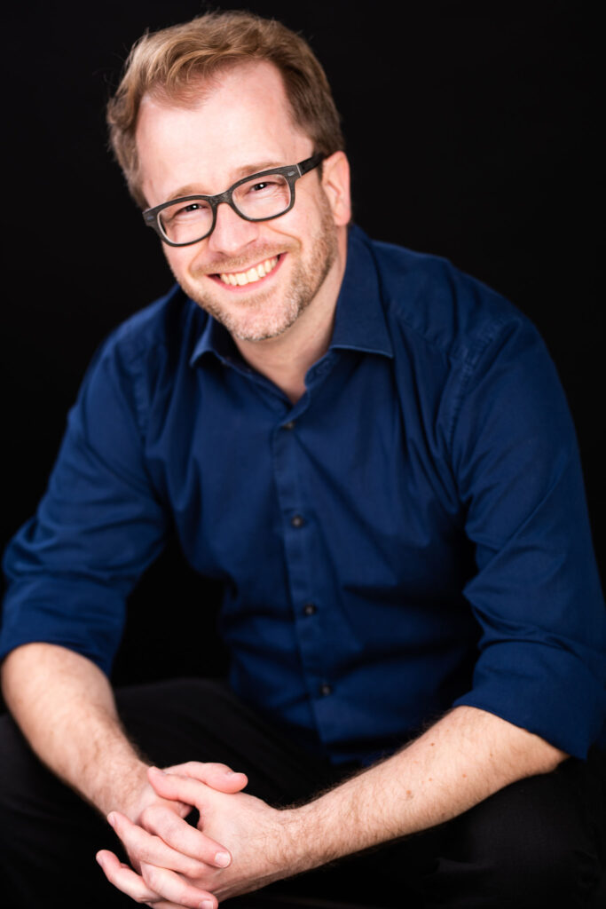 Man with golden hair, eye glasses, and dark blue collared shirt.