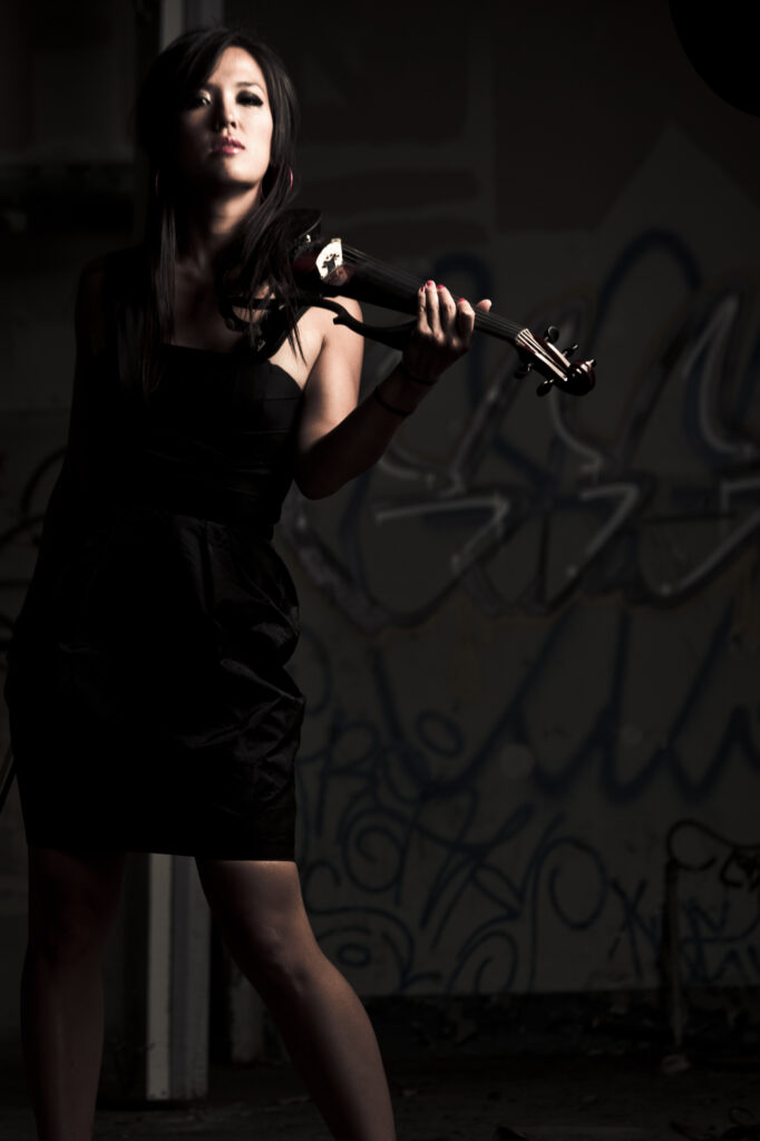 Dramatically lit Emily Hau in a black dress and holding a violin