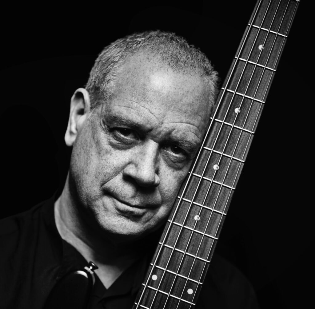 Black and white portrait of a man in dramatic lighting, face leaning towards the neck of a string instrument.